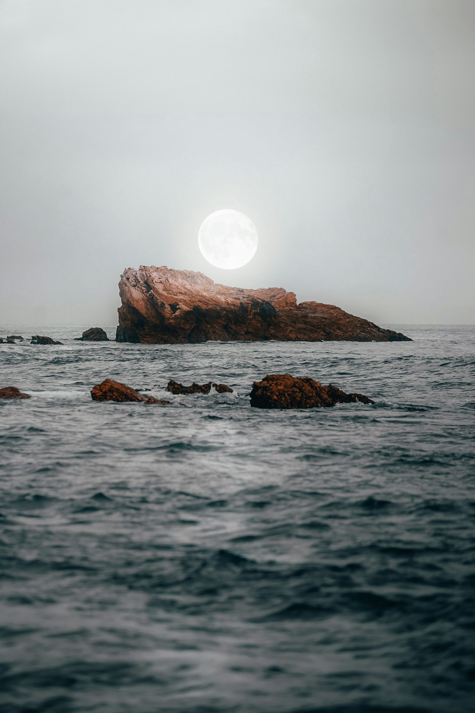 A full moon low above ocean rocks near the horizon