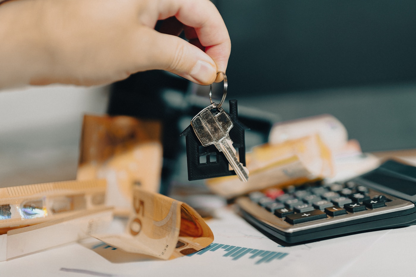 A house key held near a calculator and mortgage documents