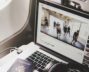 Headphones, a laptop, and a passport on an airplane tray table, showing personal electronics used during air travel