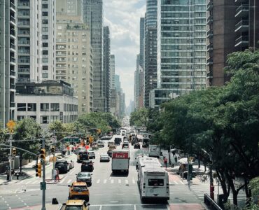 Traffic moving through a busy New York City street lined with tall buildings