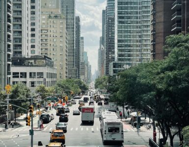 Traffic moving through a busy New York City street lined with tall buildings