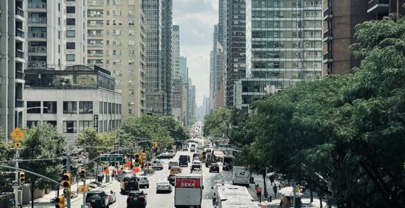 Traffic moving through a busy New York City street lined with tall buildings