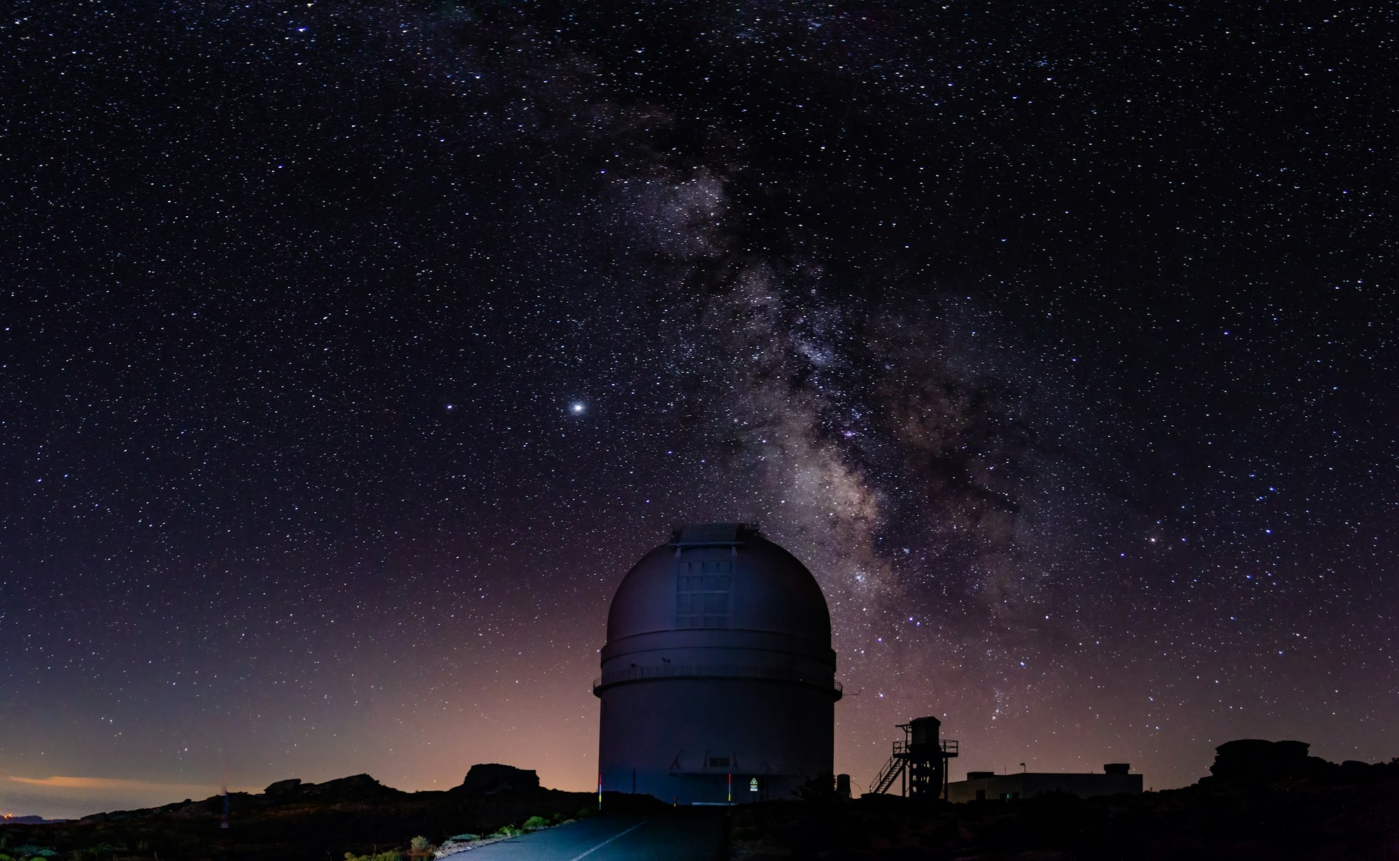 An observatory dome beneath the Milky Way in a dark night sky.