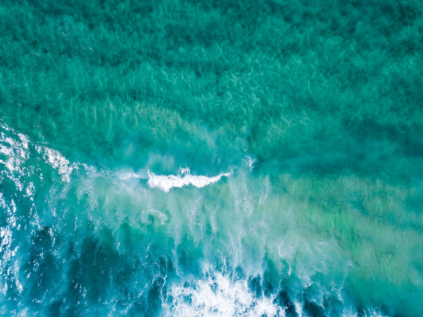 Aerial view of turquoise ocean waves moving along a coastline