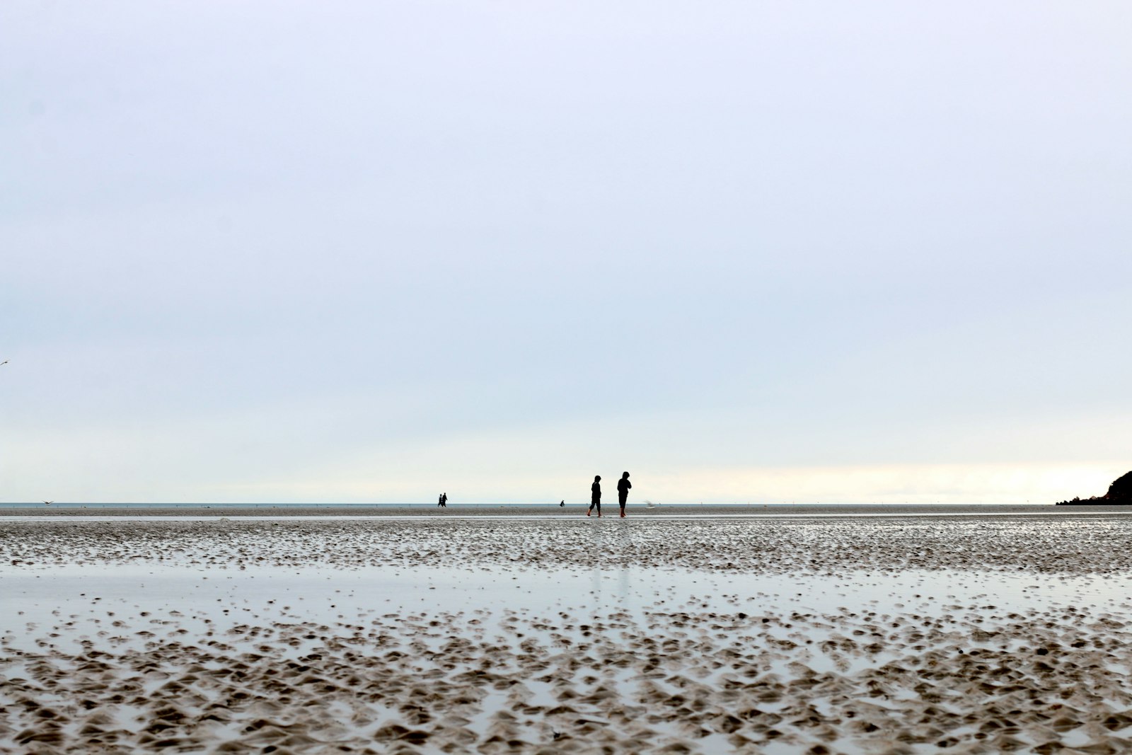 People walking across a wide wet beach exposed at low tide