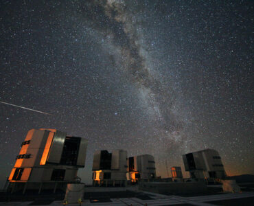A bright Perseid meteor streaks across the Milky Way above observatory telescopes at night