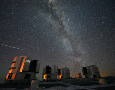 A bright Perseid meteor streaks across the Milky Way above observatory telescopes at night
