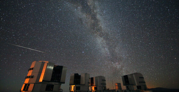 A bright Perseid meteor streaks across the Milky Way above observatory telescopes at night