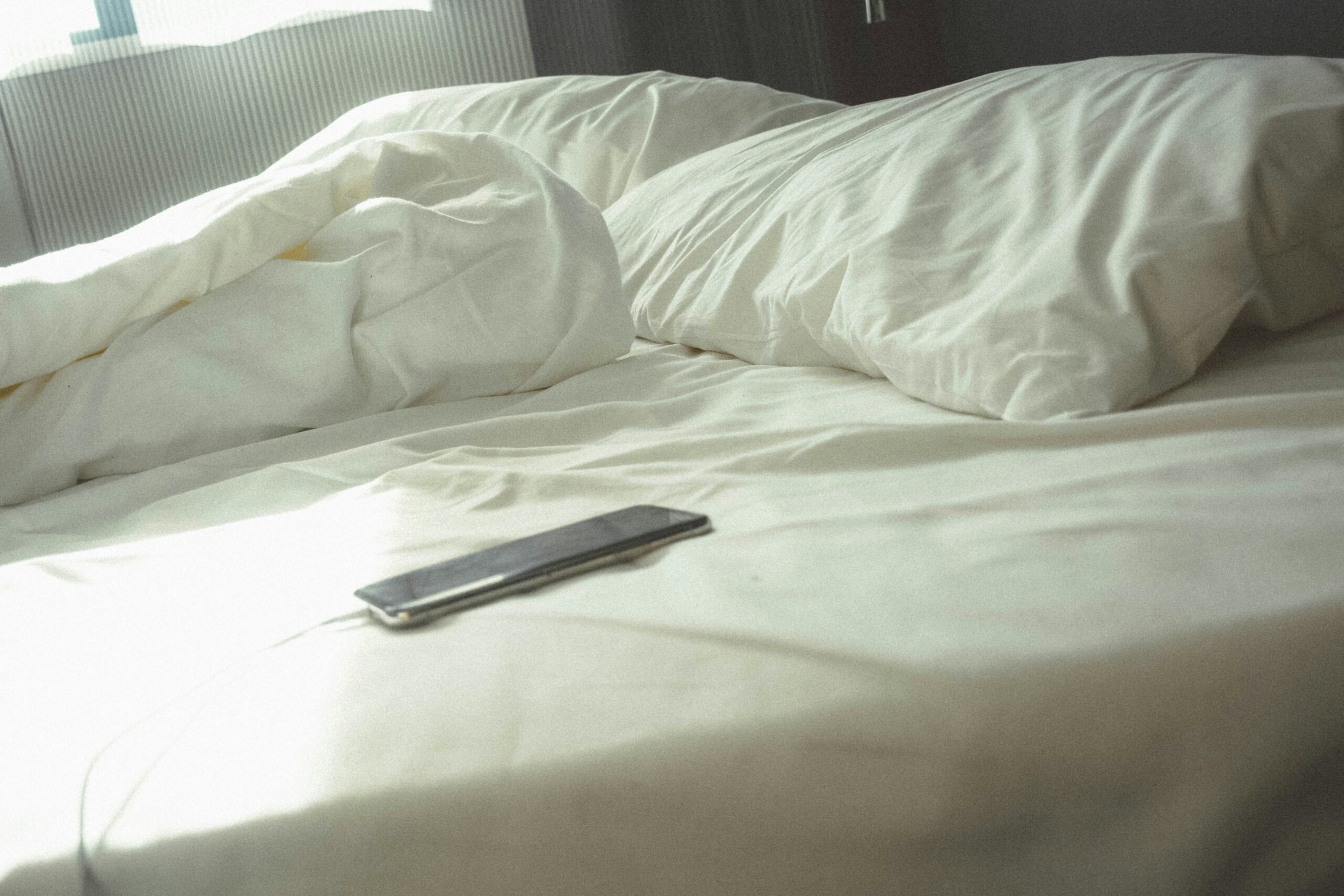 A smartphone lying on a bed near pillows in morning light.