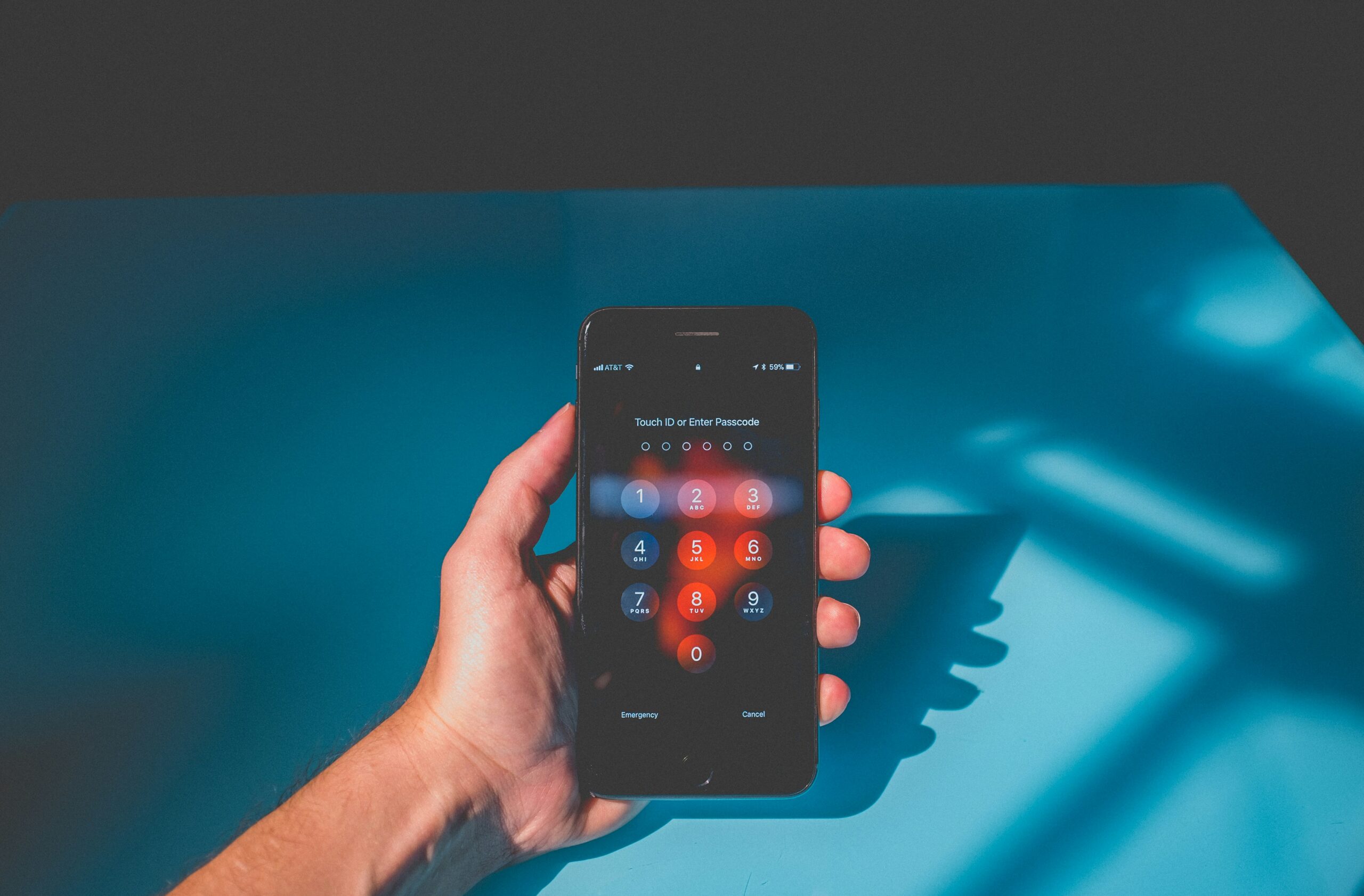A hand holding a smartphone with a passcode screen open.