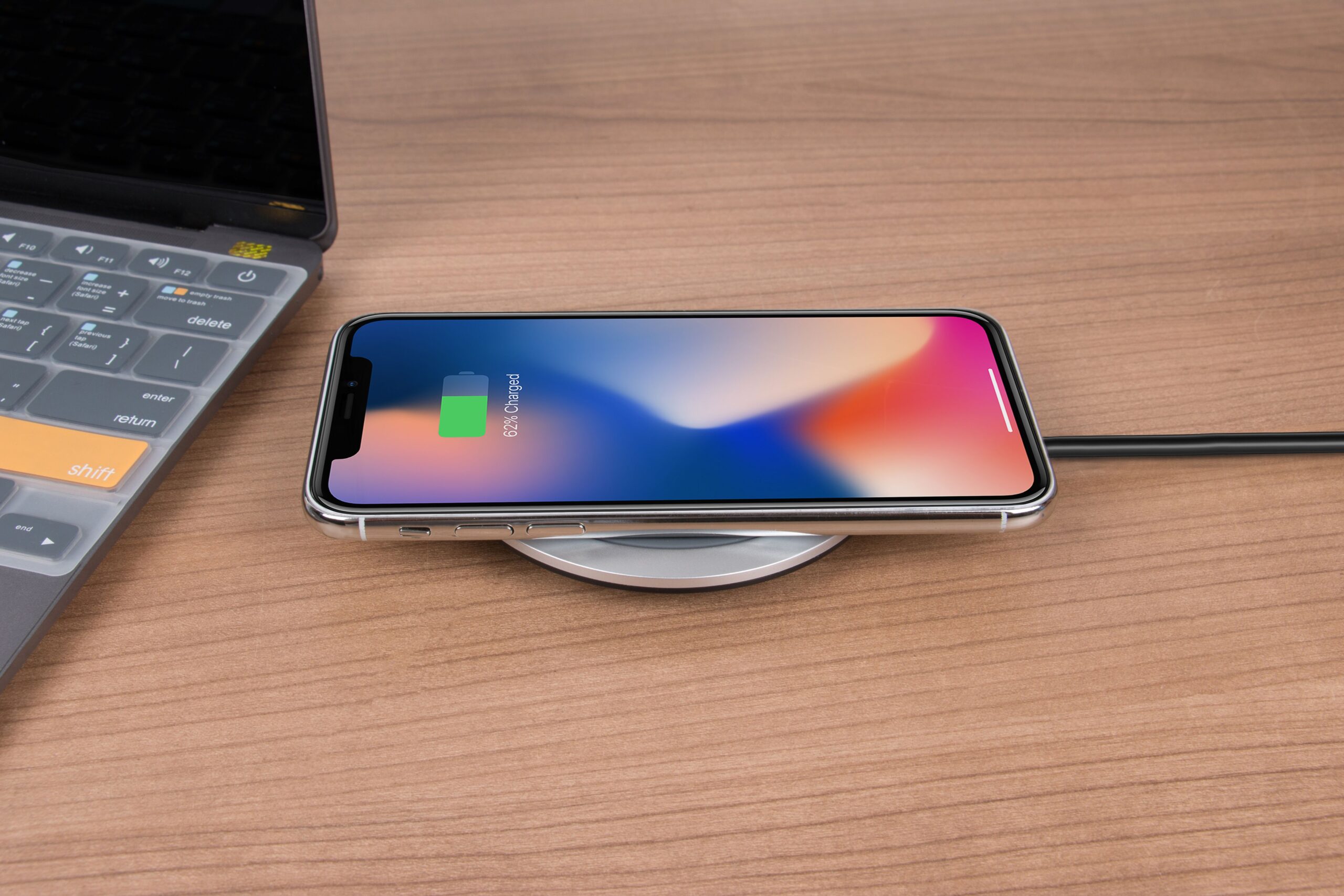 A phone charging wirelessly on a desk beside a laptop