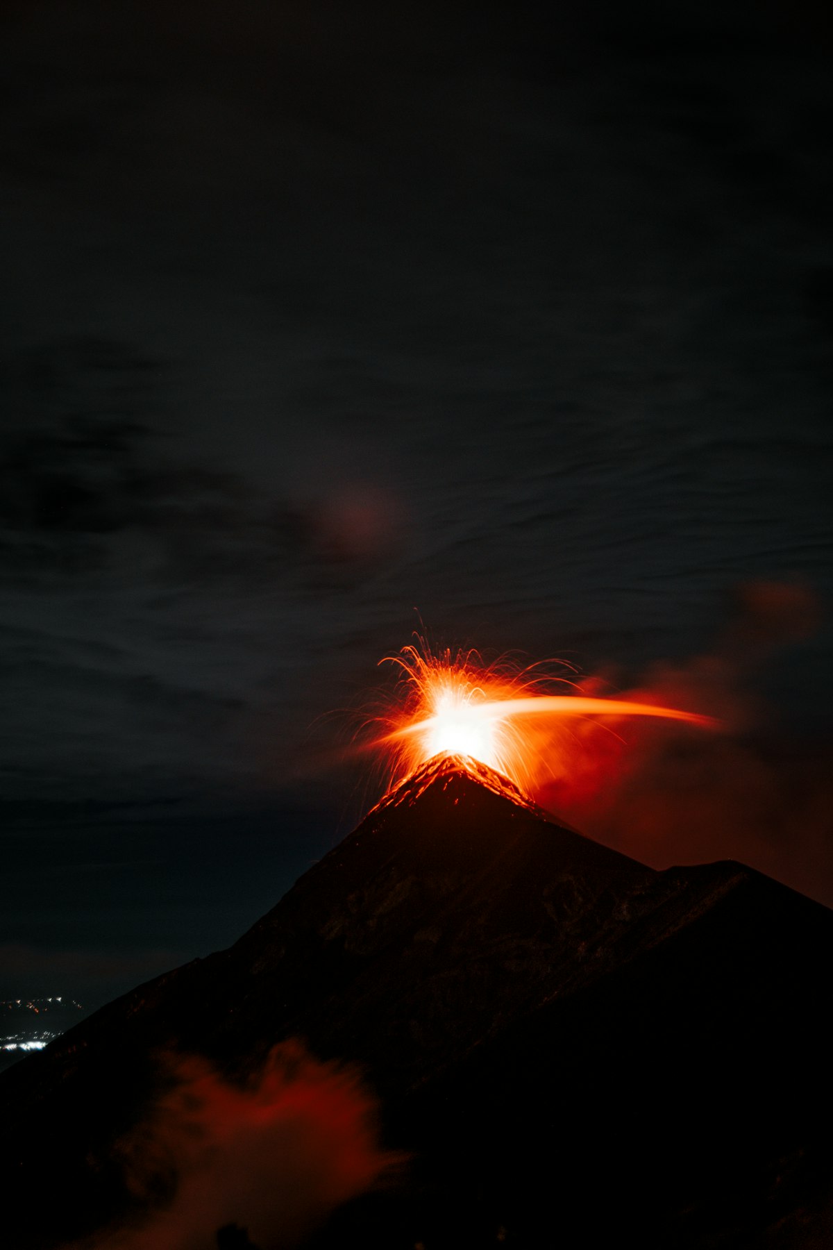 A volcano erupting at night, showing lava and glowing gas at the summit.