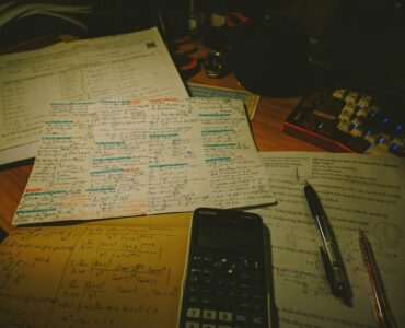 A calculator, pens, and handwritten study notes on a desk