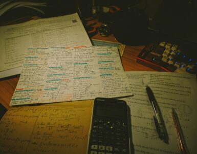 A calculator, pens, and handwritten study notes on a desk
