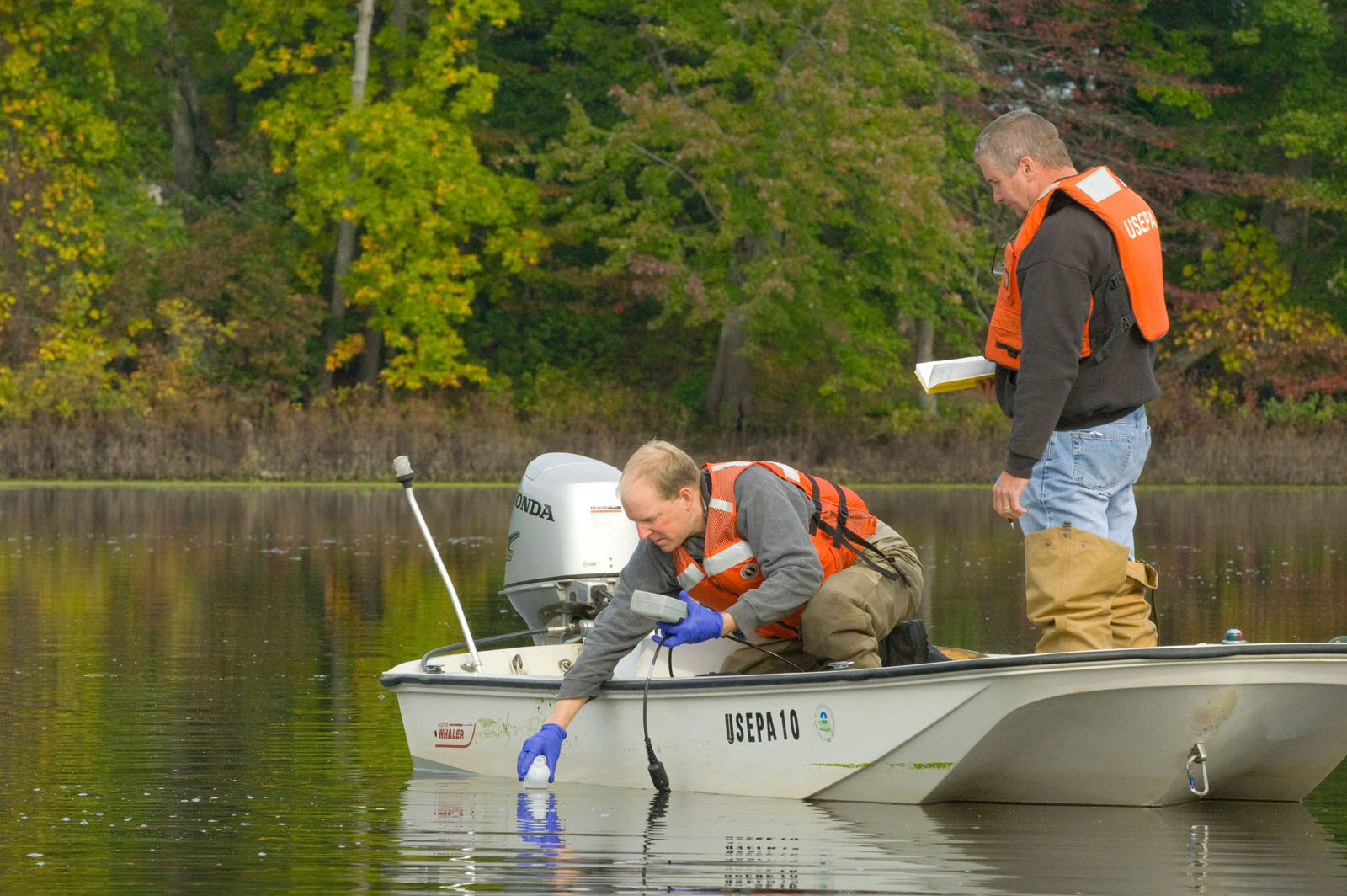 Scientists in a small boat collecting a water sample for analysis