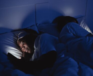 A person lying in bed at night with a phone screen lighting the room.
