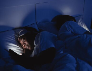 A person lying in bed at night with a phone screen lighting the room.