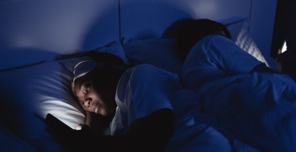 A person lying in bed at night with a phone screen lighting the room.
