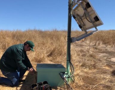 A technician services a ShakeAlert earthquake early warning sensor station in dry grassland.
