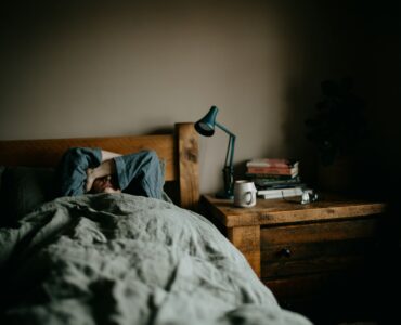 A person resting in bed in a quiet room, representing summer sleep schedules and student sleep habits.