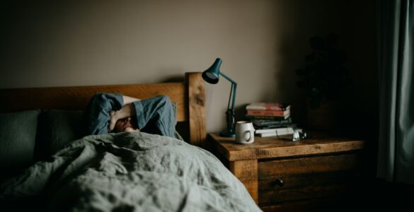 A person resting in bed in a quiet room, representing summer sleep schedules and student sleep habits.