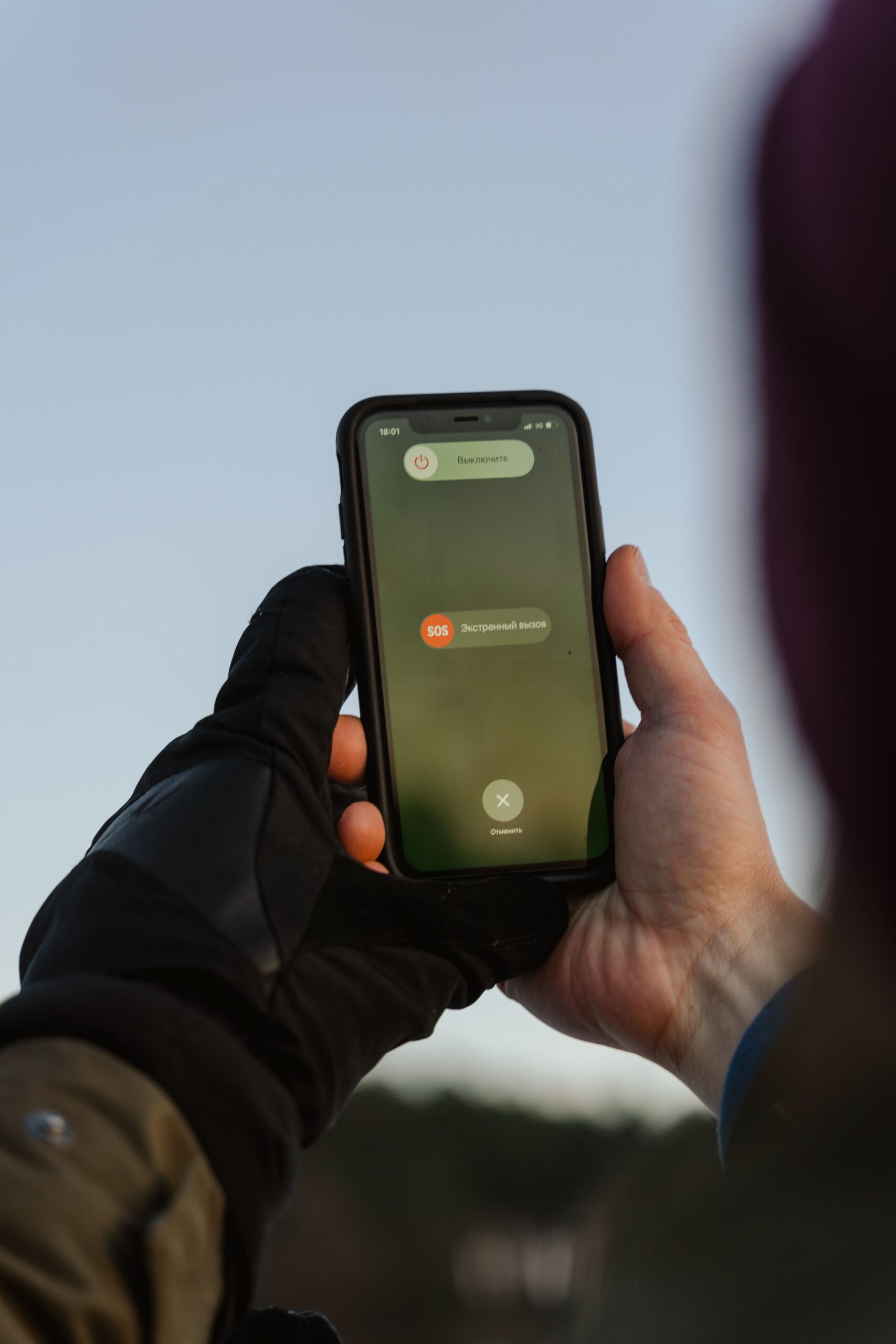 A person outdoors holding a smartphone with an emergency call option visible