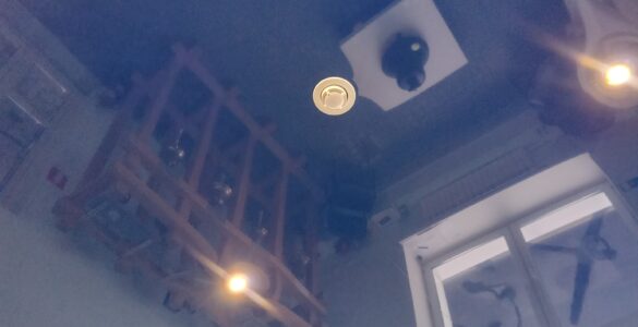 A white smoke detector mounted on a ceiling where rising smoke can reach it.