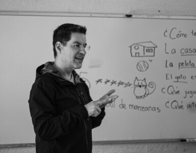 Spanish teacher explaining sentence examples on a classroom whiteboard