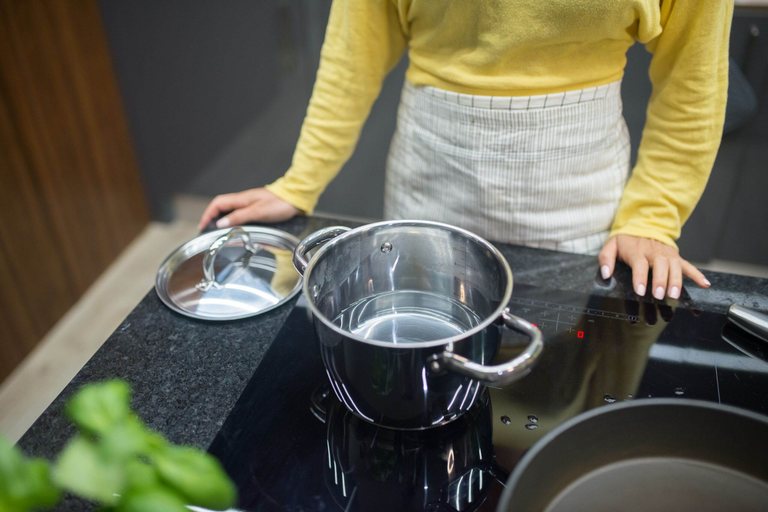 A stainless steel pot heats on a black induction cooktop in a kitchen