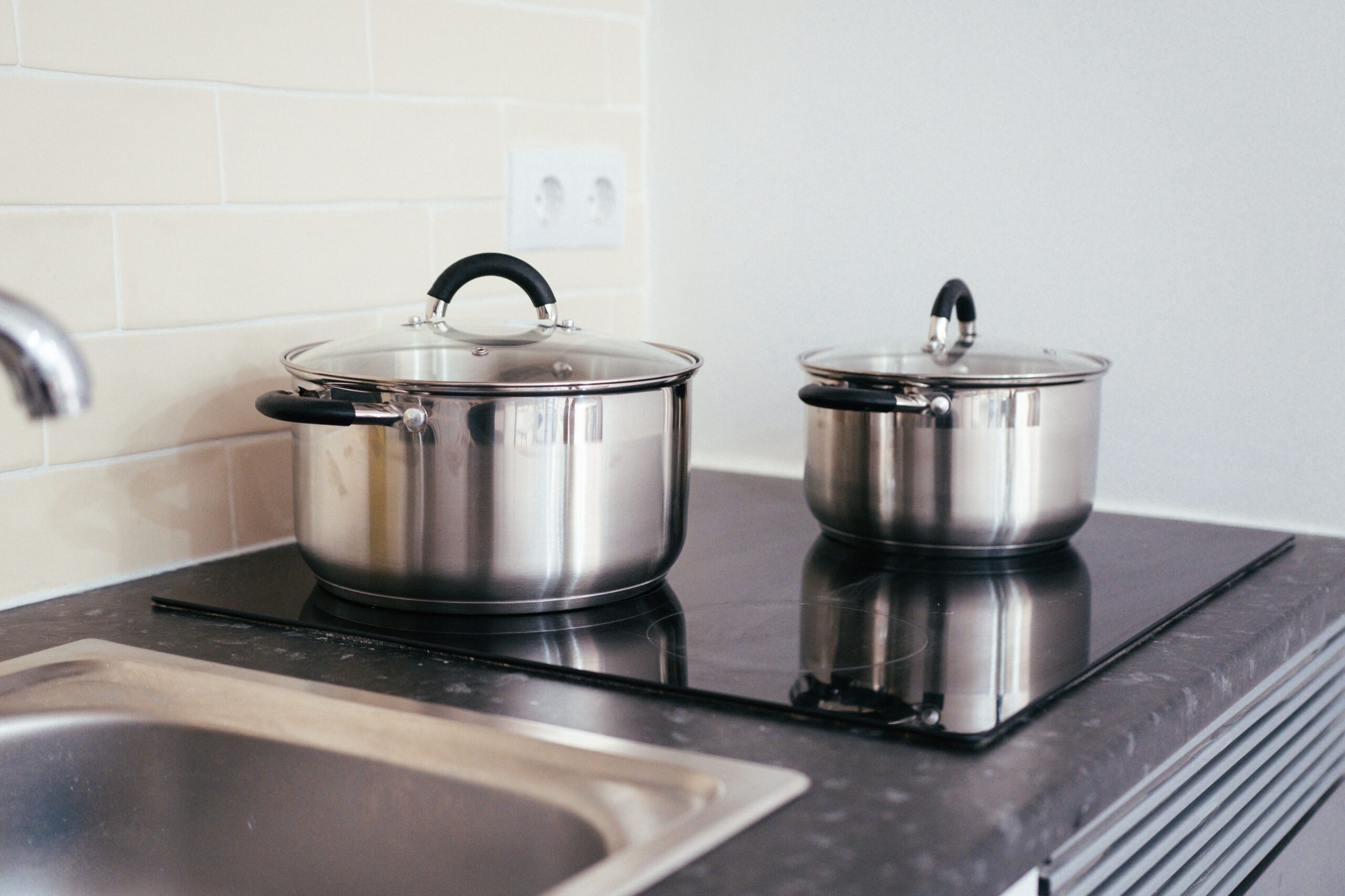 Stainless steel pots sit on a smooth black induction cooktop