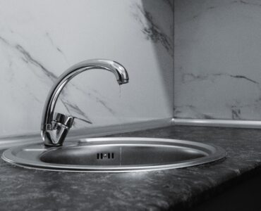A water drop falls from a chrome faucet above a stainless steel sink