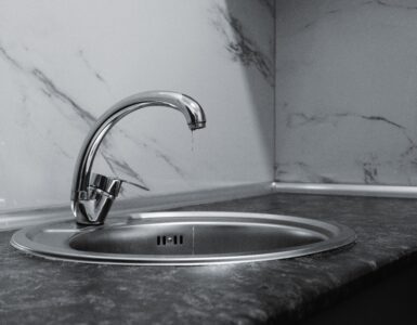 A water drop falls from a chrome faucet above a stainless steel sink
