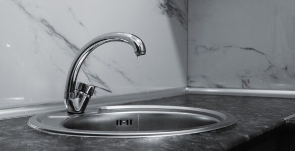 A water drop falls from a chrome faucet above a stainless steel sink