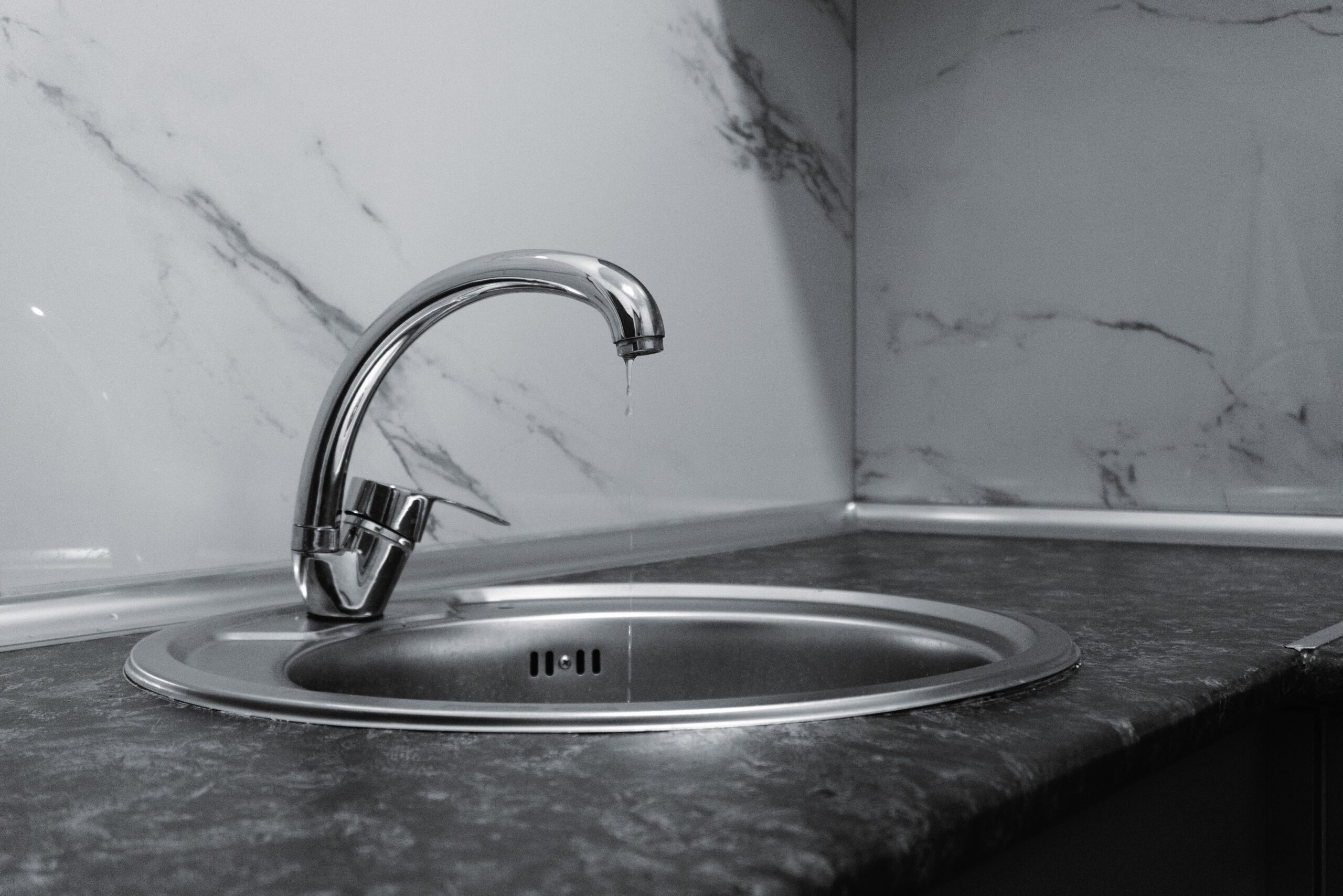A water drop falls from a chrome faucet above a stainless steel sink
