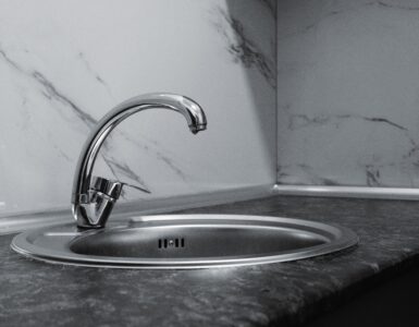 A clean stainless steel kitchen sink and faucet with a reflective metal surface