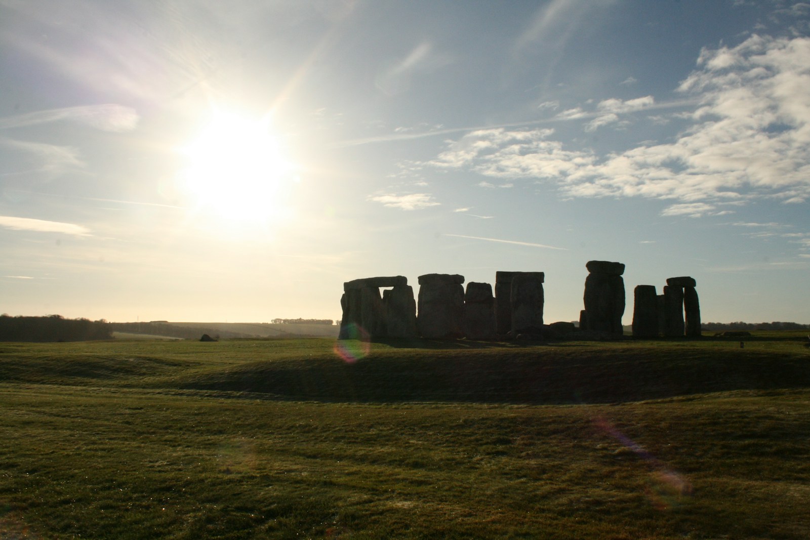 The sun rising behind Stonehenge on an open grassy landscape