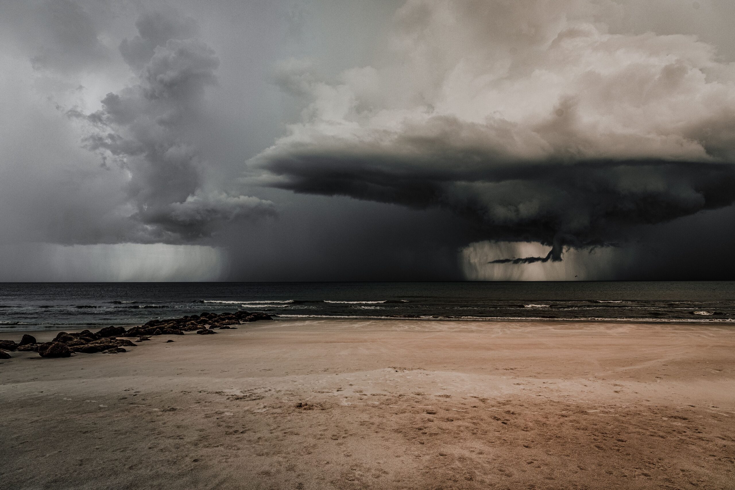 Dark storm clouds gathering over a beach and ocean before severe weather.