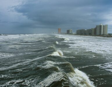 Storm-driven waves approaching a coastal city under dark clouds