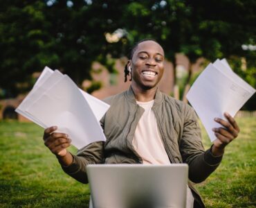 Student smiling with application papers and a laptop outdoors