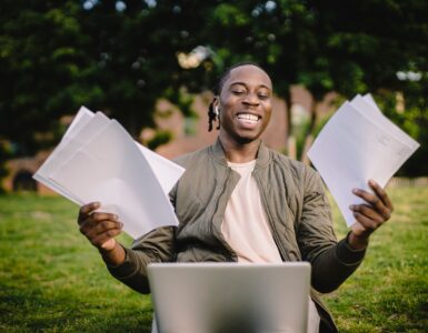 Student smiling with application papers and a laptop outdoors