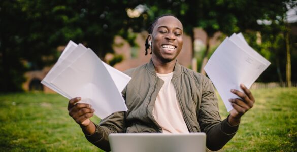 Student smiling with application papers and a laptop outdoors