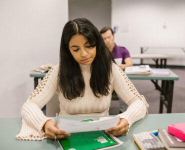 A student reviews a test paper at a classroom desk with books and a calculator nearby.