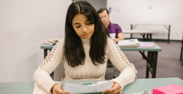 A student reviews a test paper at a classroom desk with books and a calculator nearby.