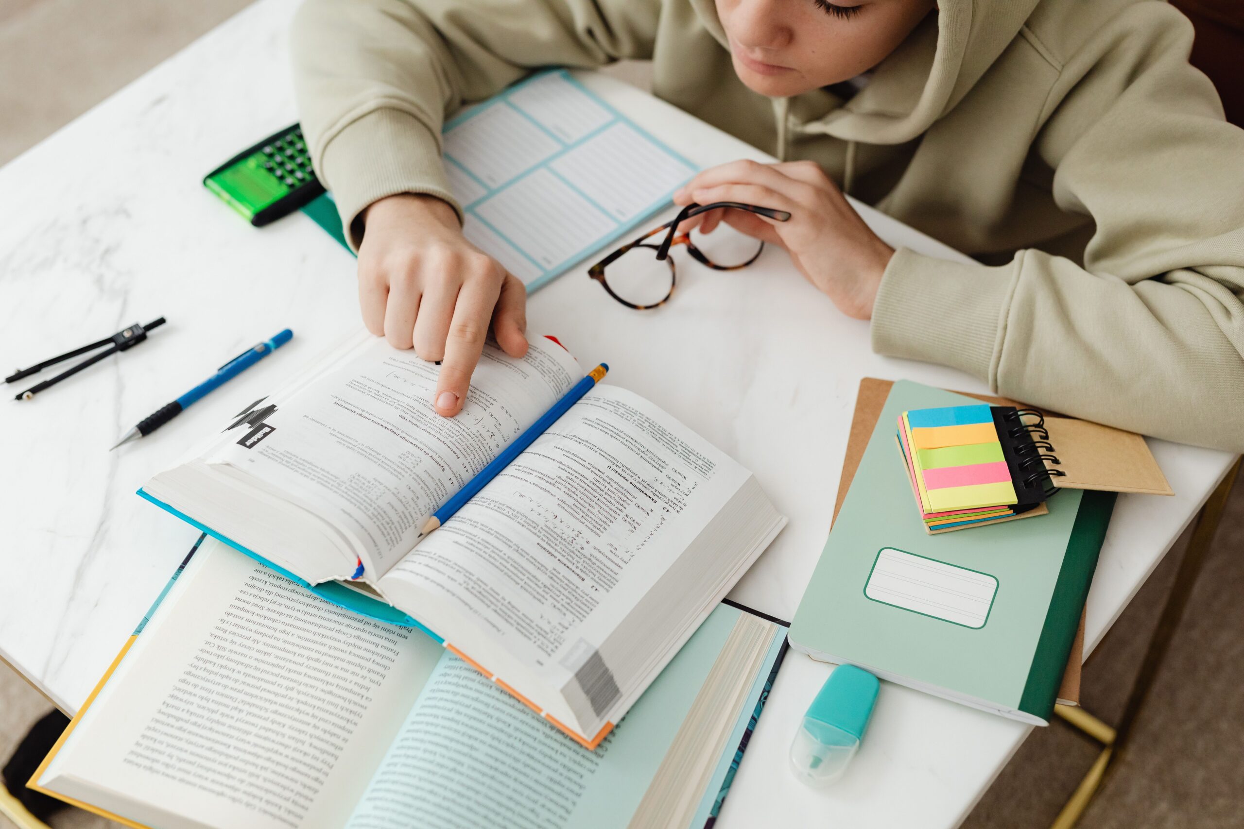 A student studying with textbooks, notes, and a calculator on a desk.