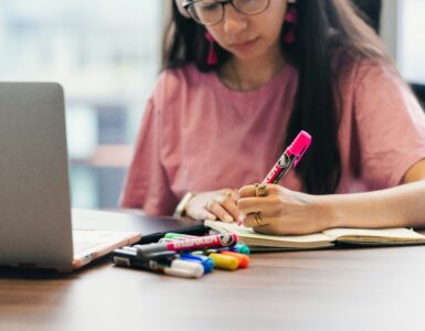 Student writing notes beside a laptop while preparing for a test.