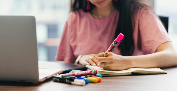 Student writing notes beside a laptop while preparing for a test.