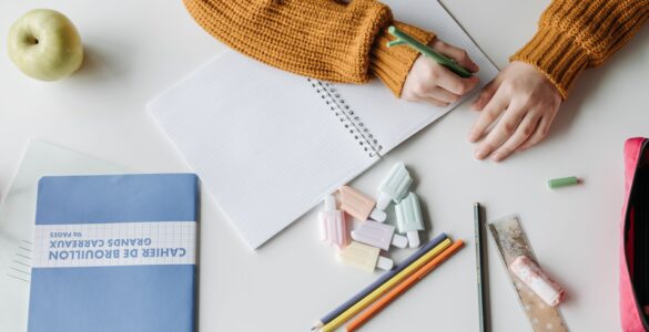 A student writes handwritten notes while developing analysis for an essay paragraph.