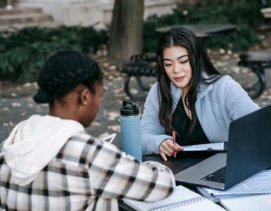 Two students review papers and a laptop while planning college coursework.