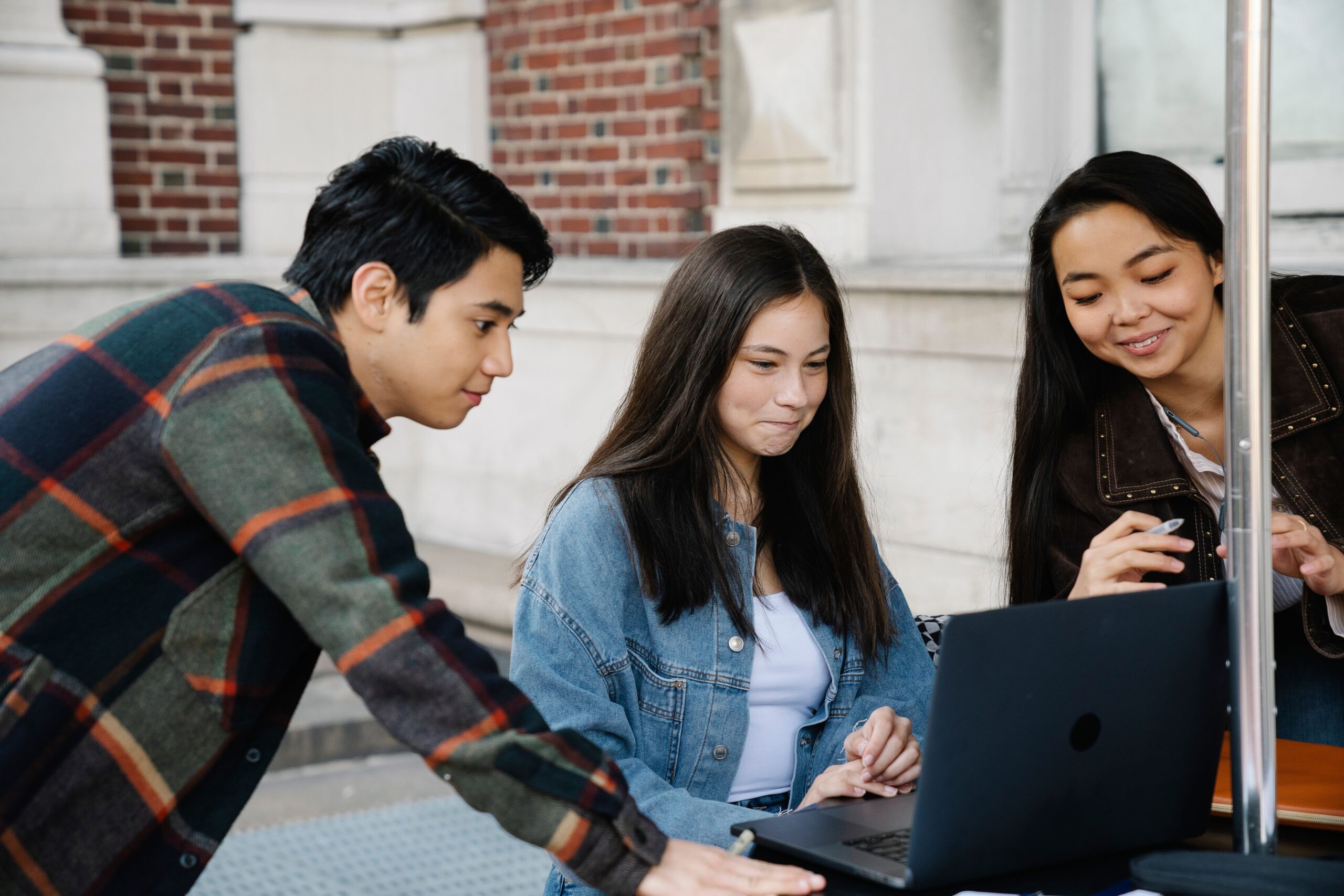 Three students reviewing information on a laptop outdoors