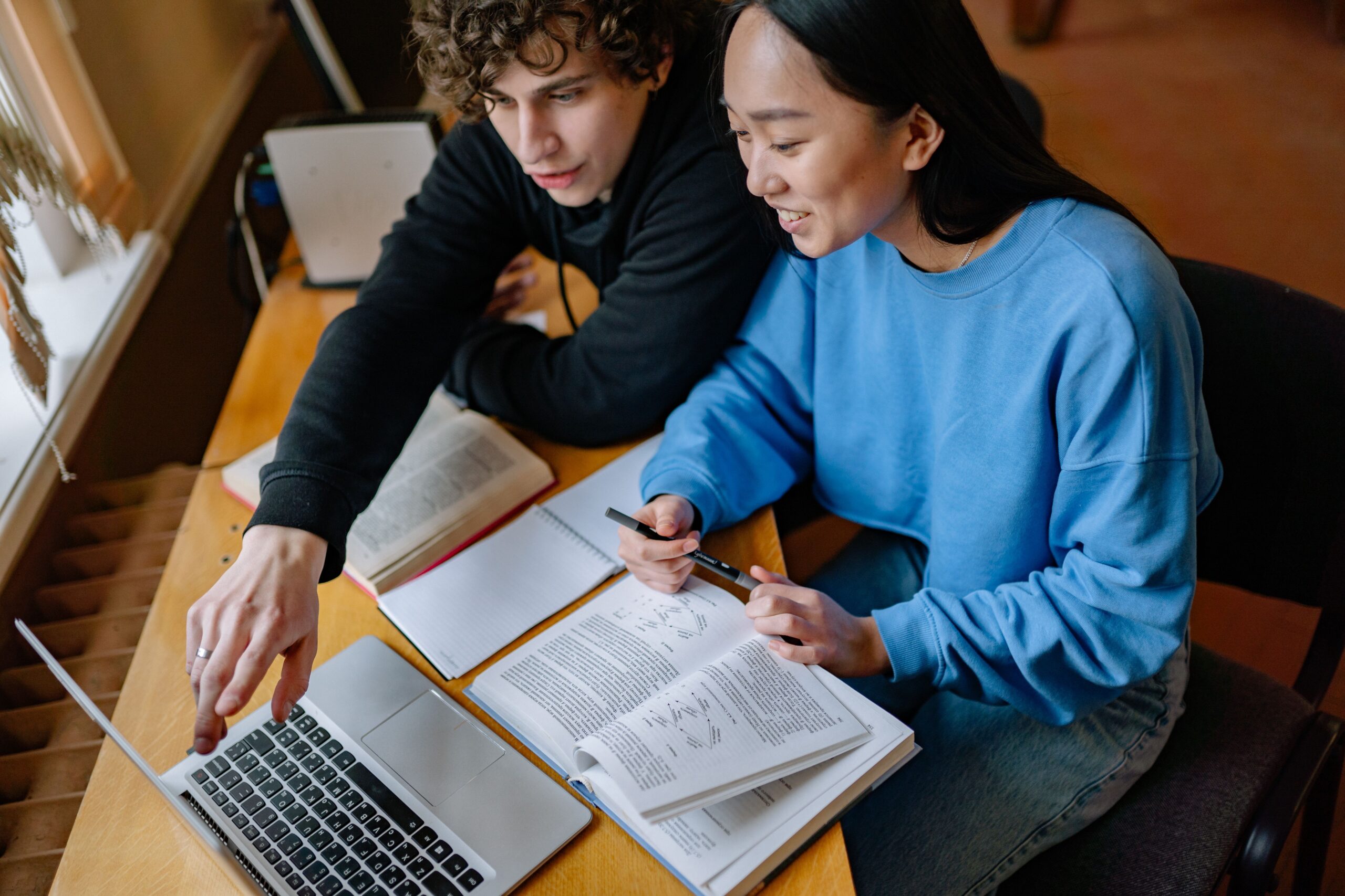 Two students planning applications with books and a laptop